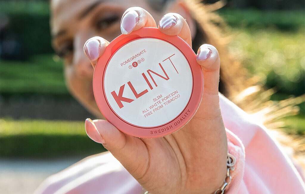 Woman wearing pink holding KLINT nicotine pouch in pomegranate flavour